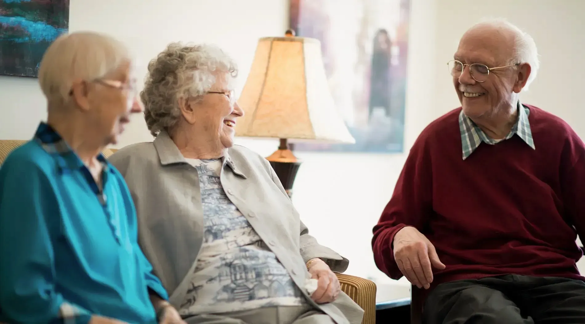 Three older adults chatting and laughing together in a sitting room